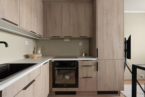 A modern kitchen with wooden cabinets, a black stove, and a built-in oven. - Bright & Cozy Studio Apartment (Tromsø)