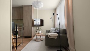 Een moderne woonkamer met een grijze bank, een ronde salontafel, een flatscreentelevisie en een vloerlamp.