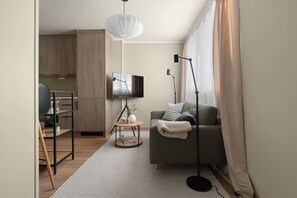 A modern living room with a grey sofa, a round coffee table, a flat-screen TV, and a floor lamp. - Bright & Cozy Studio Apartment (Tromsø)