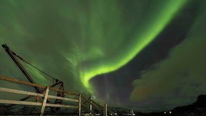 Une scène nocturne avec des aurores boréales au-dessus d’un paysage enneigé et d’une structure en bois.