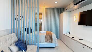 A modern hotel room with a bed, a sofa, a TV, and a partition with vertical slats.