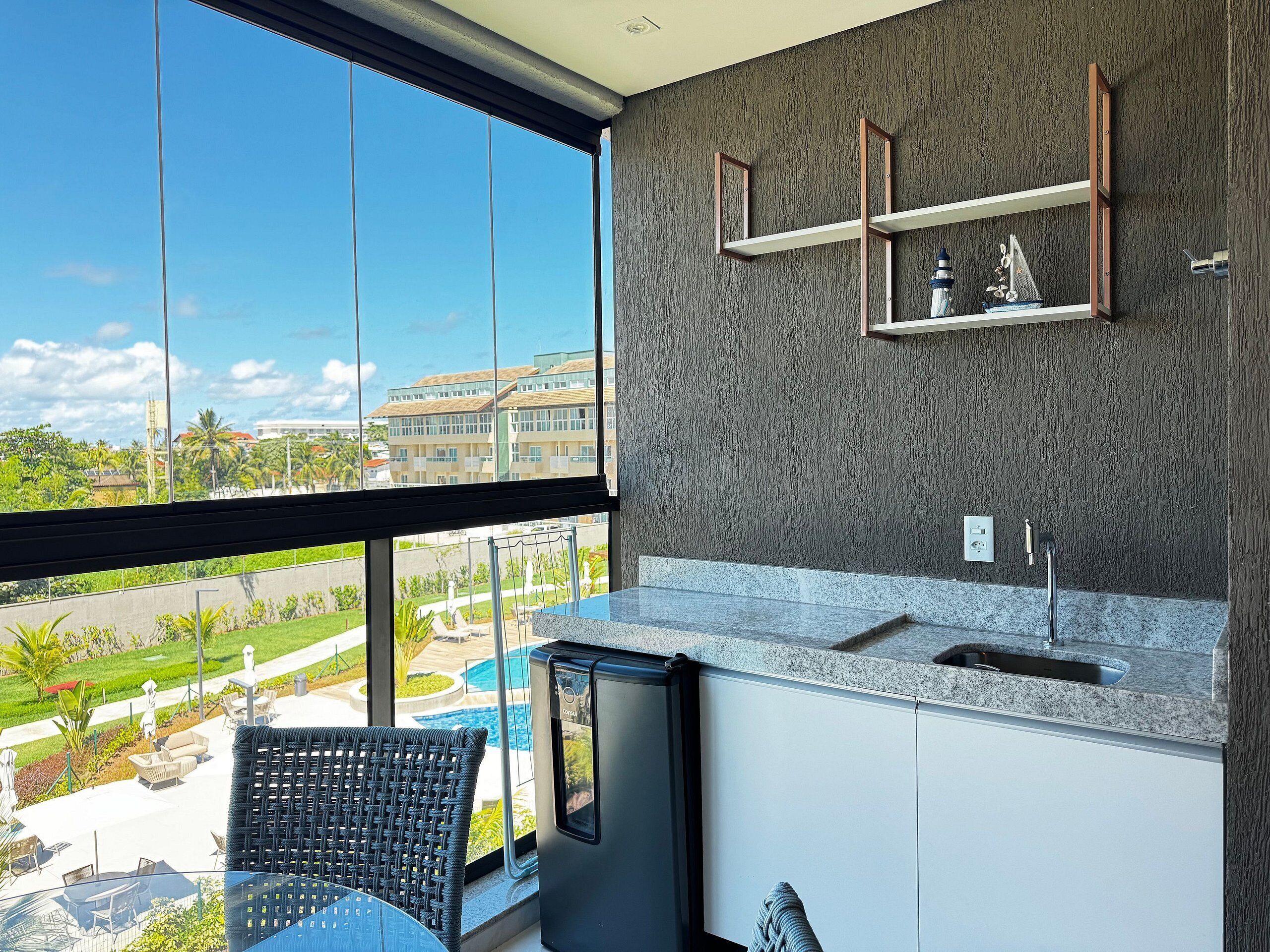 Una cocina moderna con un ventanal grande, un lavamanos integrado y vistas a una piscina y edificios.