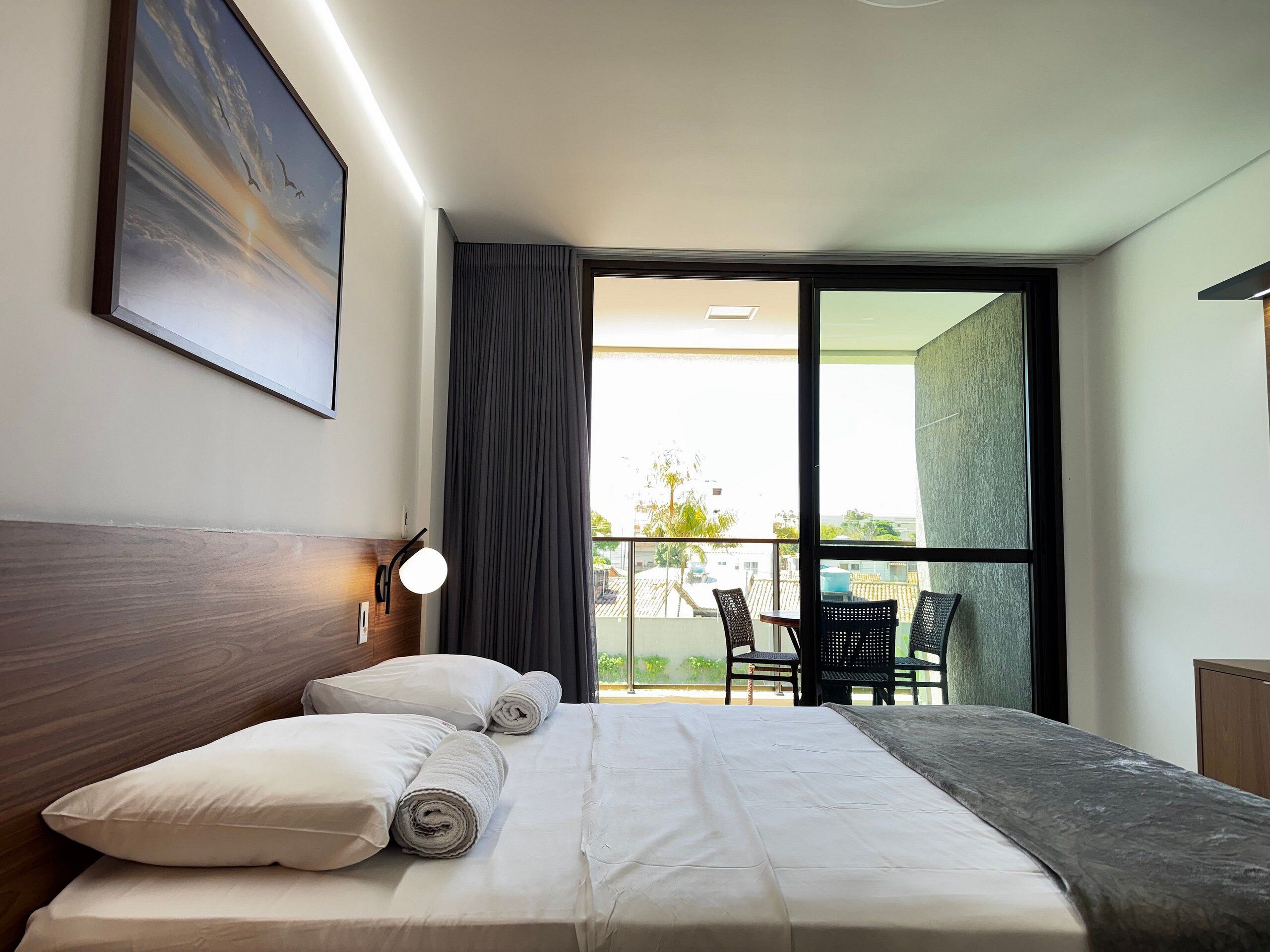 Habitación de hotel con cama, un cuadro, una ventana con cortinas y vistas al exterior.