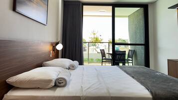 Habitación de hotel con cama, un cuadro, una ventana con cortinas y vistas al exterior.