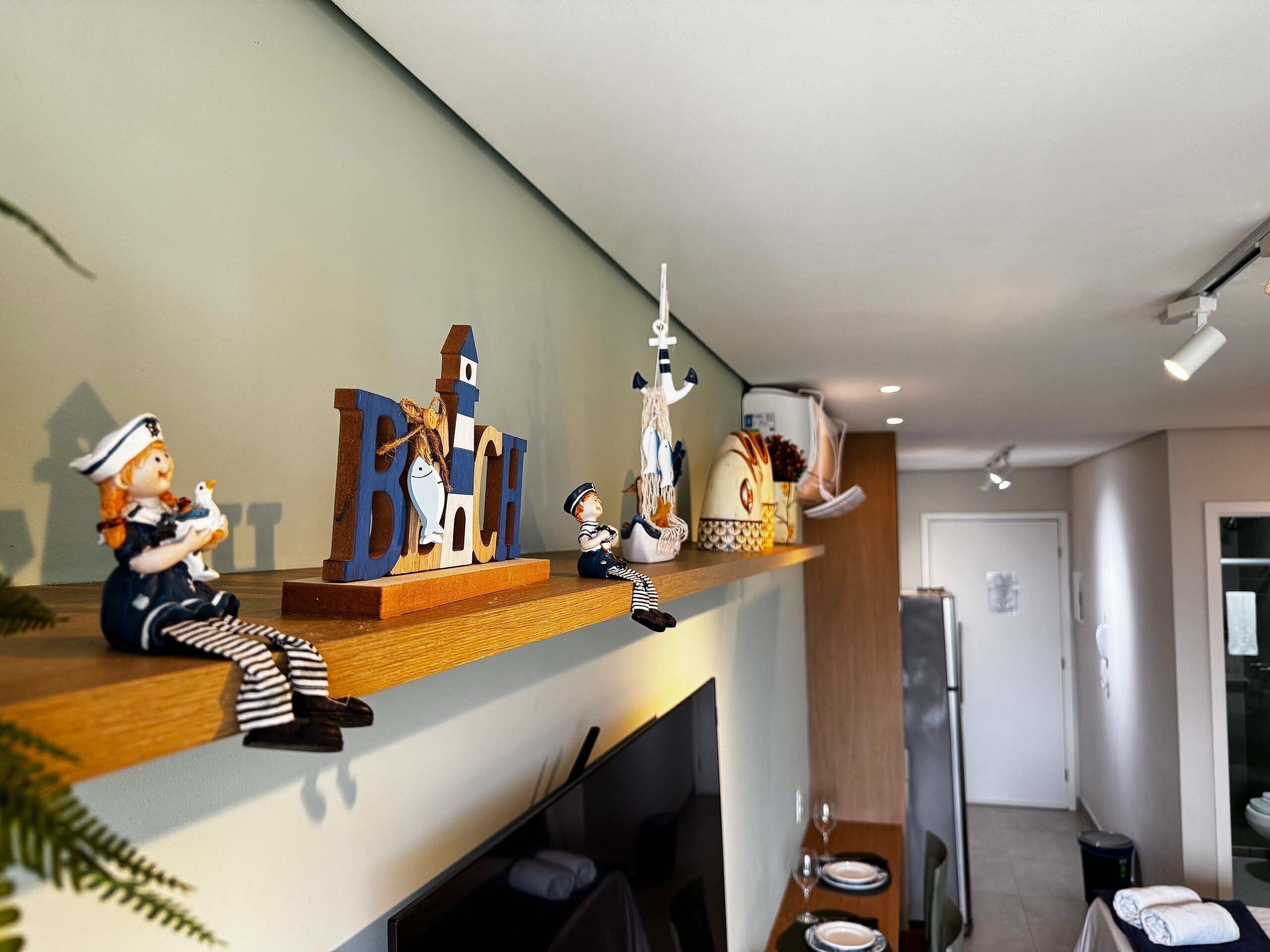Un área de cocina con un estante de madera que exhibe varios objetos decorativos, un televisor y una vista parcial de un baño.