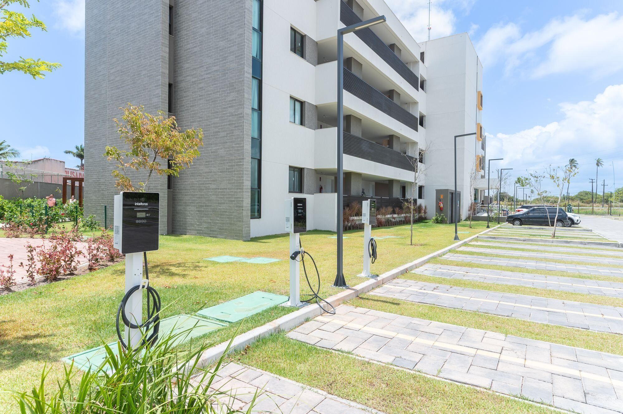 Um edifício moderno com área de estacionamento, estações de carregamento para veículos elétricos e um gramado bem cuidado.