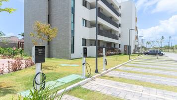 Um edifício moderno com área de estacionamento, estações de carregamento para veículos elétricos e um gramado bem cuidado.