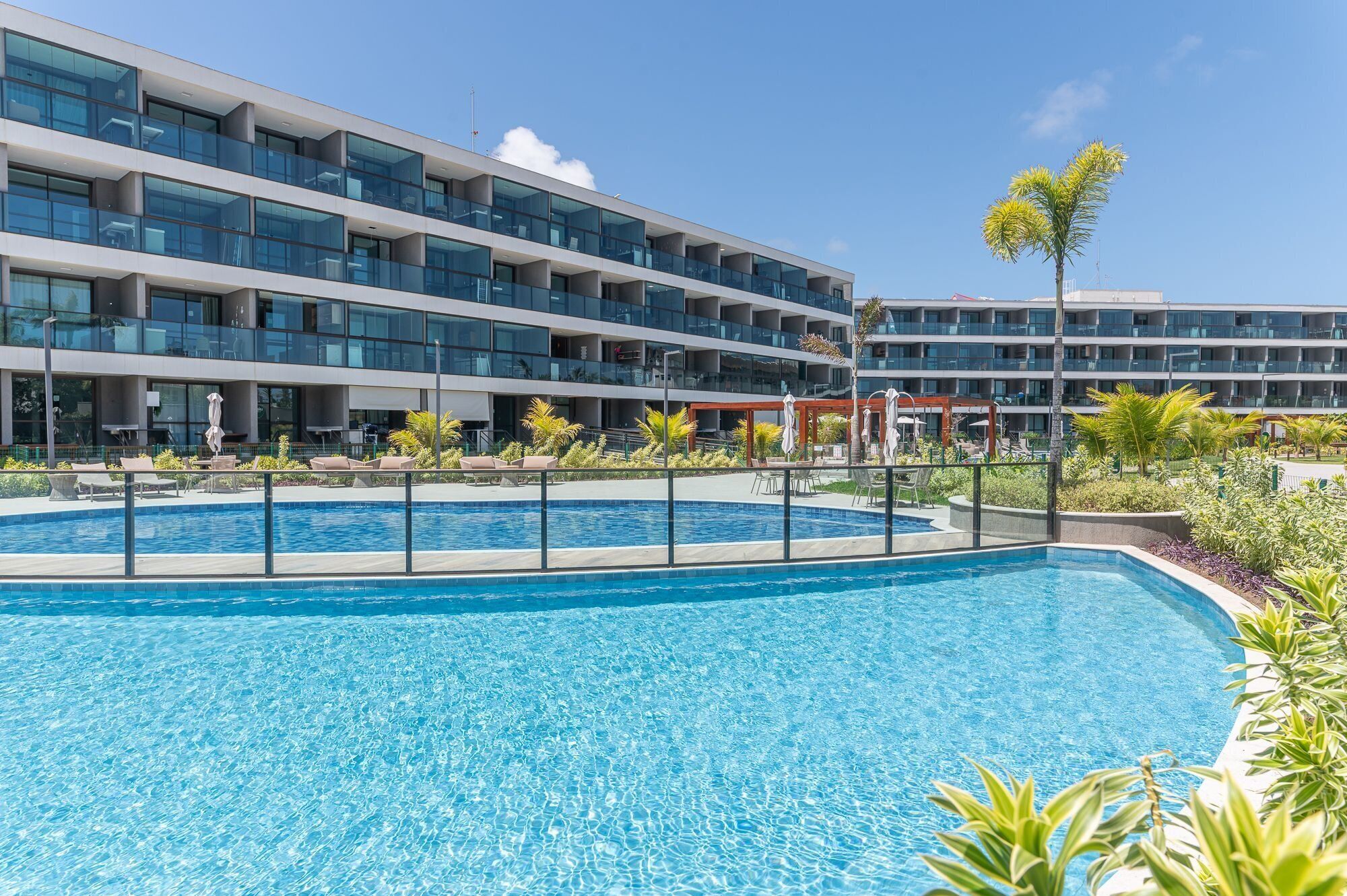 A modern hotel with a swimming pool, multiple balconies, and outdoor seating areas.