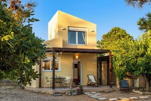 Ein modernes, zweistöckiges Haus mit überdachter Terrasse, Sitzgelegenheiten im Freien und einem Garten.