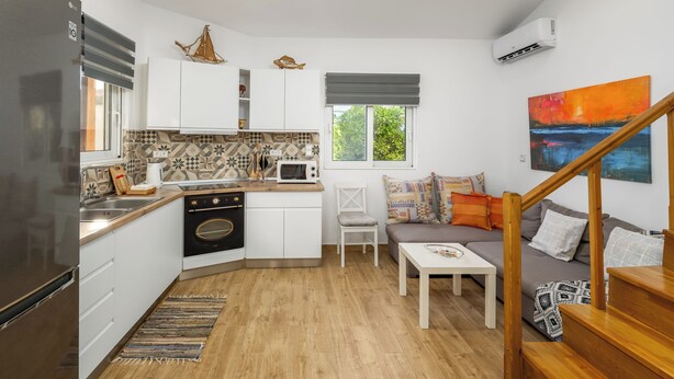Une cuisine compacte dotée d’appareils électroménagers modernes, un coin repas avec une table en bois et un espace de vie comprenant un canapé et un tableau.