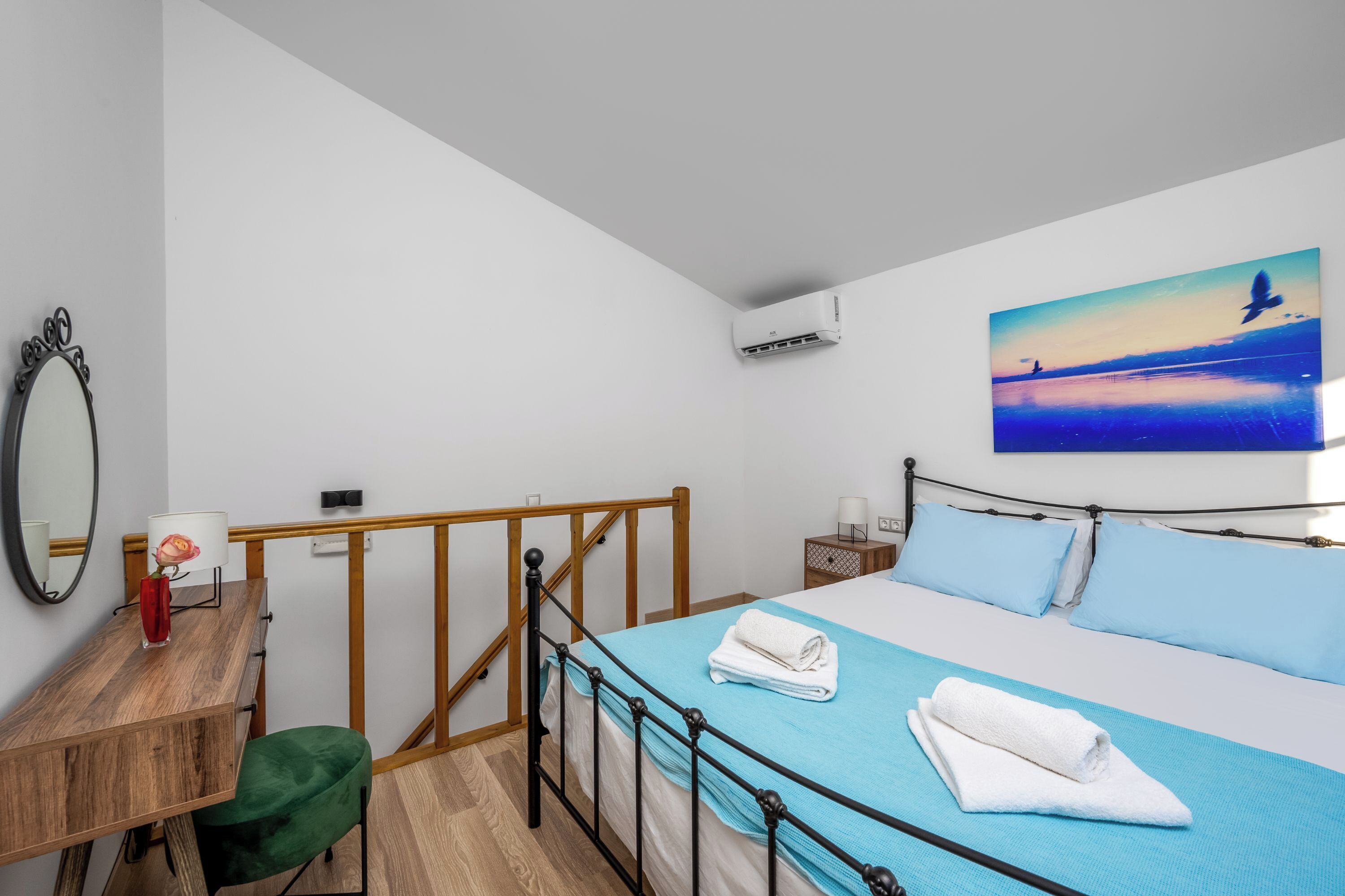 Ett hotellrum med en säng, ett skrivbord, en stol, en spegel, en luftkonditionering och en tavla som föreställer en fågel som flyger över vattnet.