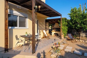 Eine Terrasse mit Tisch und Stühlen, eine hölzerne Pergola und eine Steinmauer.