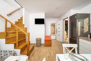 Um apartamento moderno com escada de madeira, televisão de tela plana, cozinha com geladeira de aço inoxidável e área de jantar com mesa e cadeiras.