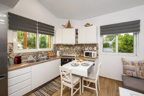 Uma cozinha compacta com fogão, micro-ondas e pia, uma mesa de jantar com cadeiras e grandes janelas com cortinas.