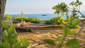 Un hamac est tendu entre deux arbres, d’où l’on a une vue sur une étendue d’eau, avec un bateau qui se profile à l’horizon.