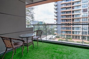 Uma varanda com uma mesa redonda e cadeiras de vime, com vista para um edifício moderno com varandas.