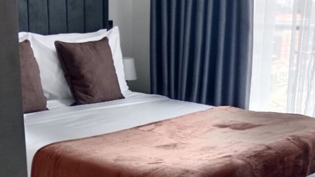 Une chambre à coucher moderne avec un lit, un banc recouvert d’un tissu gris et un rideau bleu foncé.