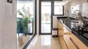 Une cuisine moderne avec un plan de travail noir, des appareils en acier inoxydable et une vue sur l’extérieur grâce à une porte vitrée.