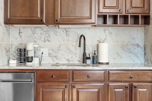 A kitchen with wooden cabinets, a marble backsplash, a stainless steel dishwasher, and a coffee maker.