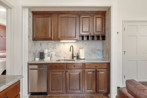 A kitchen with wooden cabinets, a stainless steel dishwasher, a marble backsplash, and a built-in sink.