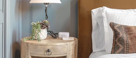 A wooden bedside table with a lamp, a small plant, and a power strip.