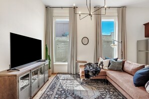 A modern living room with a flat-screen TV, a sofa, a coffee table, and a patterned rug.