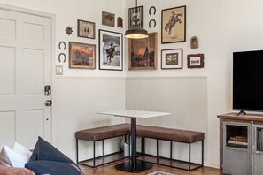 A room with a white door, a bench table, and a television on a cabinet.