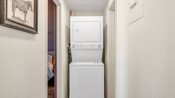 Un espace buanderie avec une machine à laver et un sèche-linge superposés, un tableau encadré accroché au mur et une porte donnant sur une autre pièce.