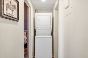 A laundry area with a stacked washer and dryer, a framed picture on the wall, and a door leading to another room.
