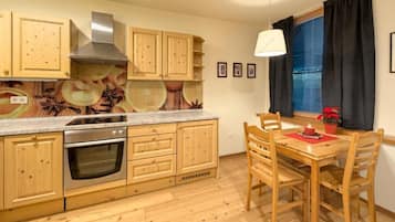 Una cocina con armarios de madera, un horno de acero inoxidable, una mesa de comedor con sillas y una ventana con cortinas.