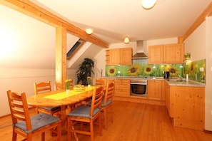 A kitchen with wooden cabinets, a dining table with chairs, and a sunflower mural on the wall.