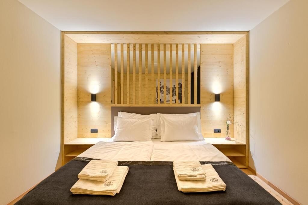 A hotel room with a wooden headboard, two bedside tables, a bed with white linens, and two wall-mounted lamps.