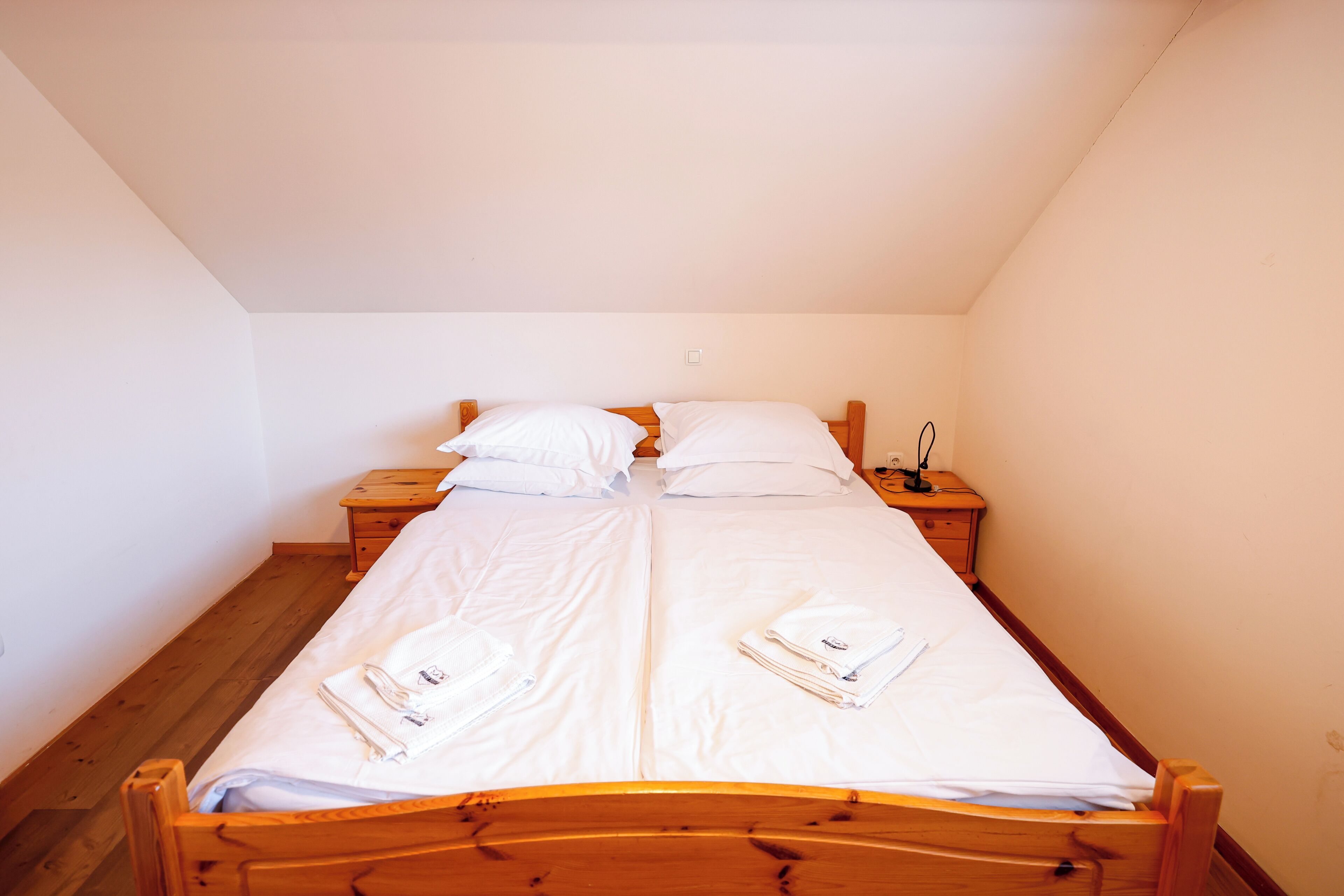 A single bed with white linens and towels, wooden headboard, and a nightstand with a lamp.