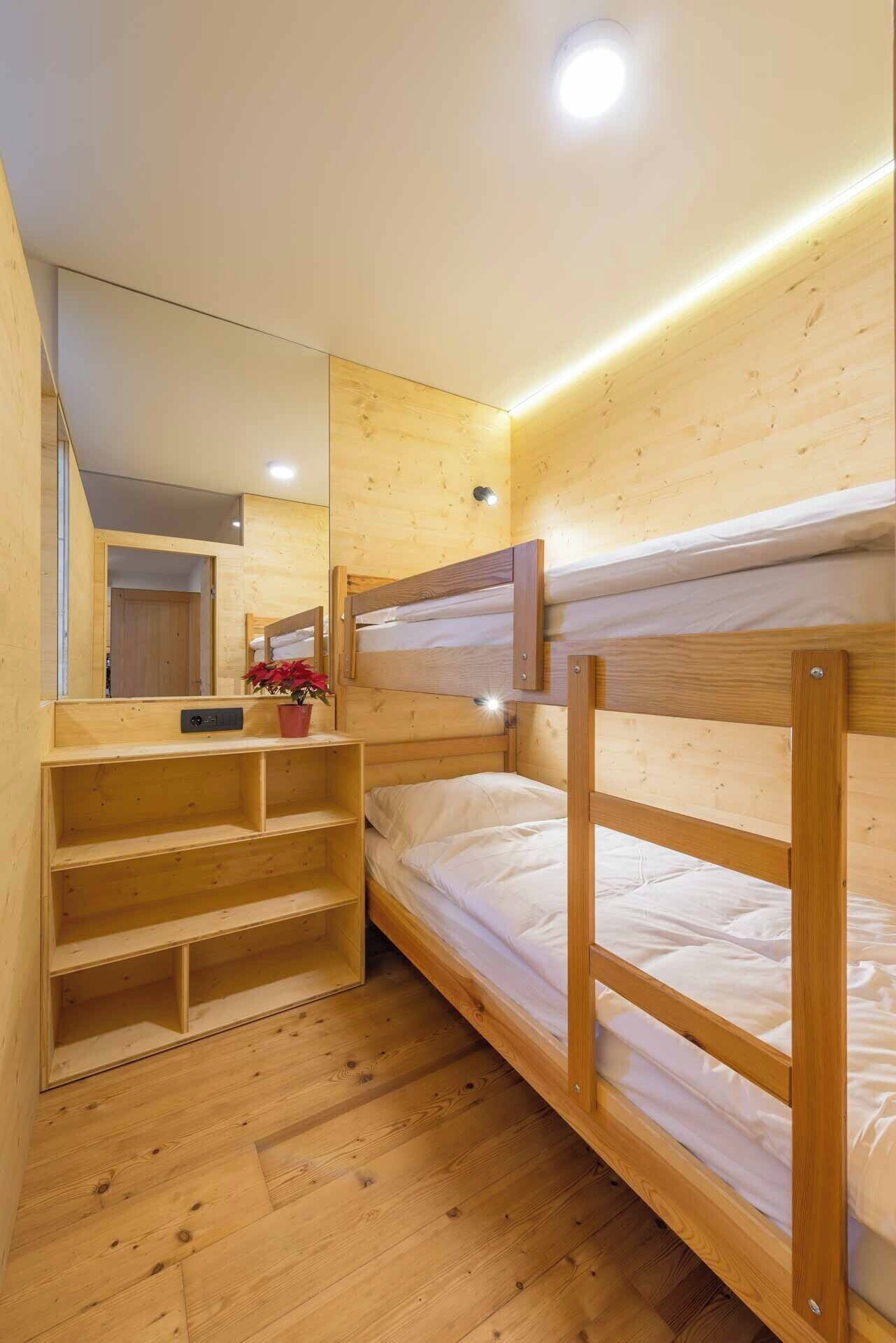 Ein kleines Zimmer mit Etagenbett, Spiegel und Ablagefläche mit einem Blumentopf.