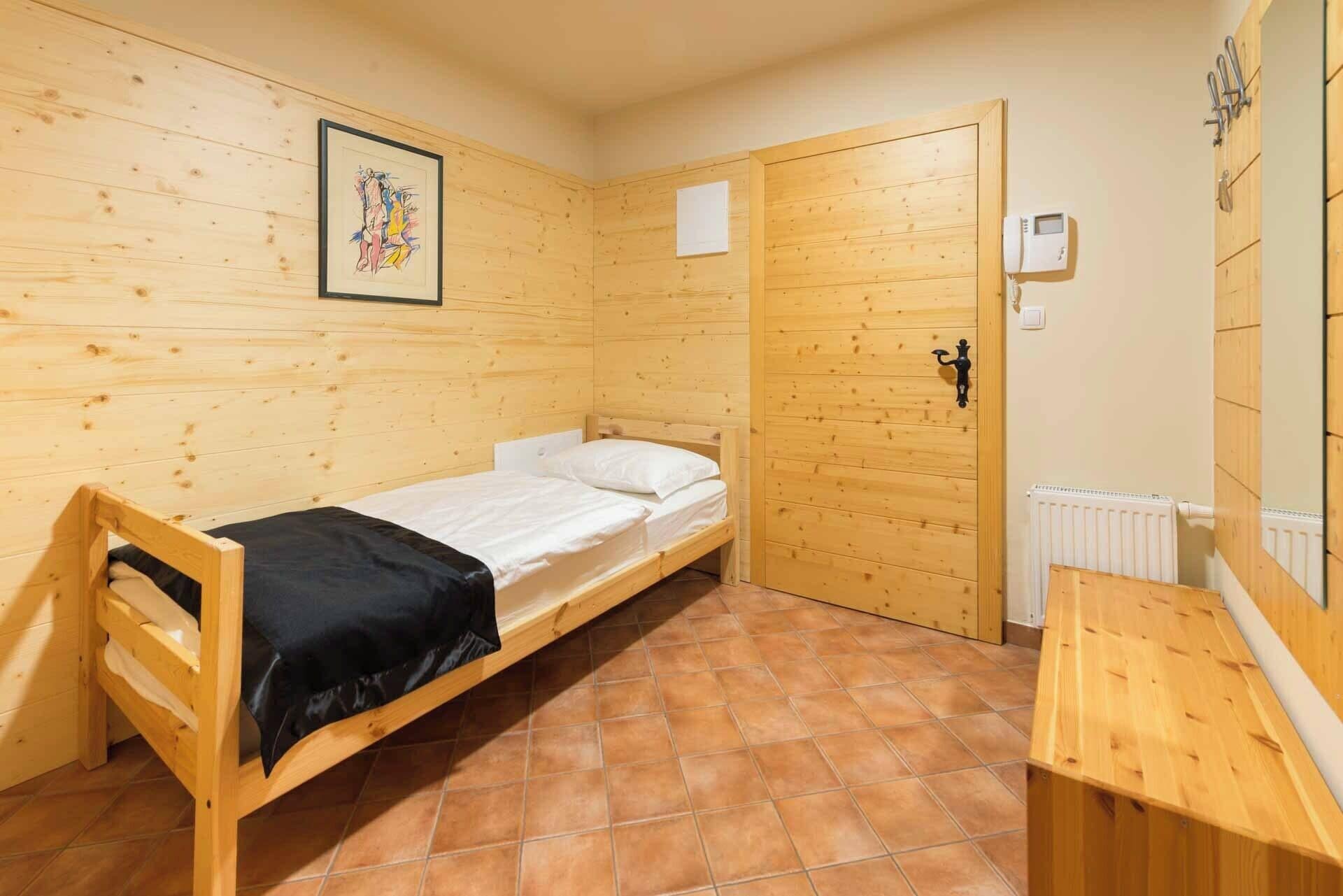 Ein Einzelbett mit schwarzer Decke, eine Holztür, ein weißer Heizkörper und ein kleiner Tisch.