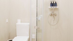 A modern bathroom with a glass-enclosed shower, a toilet, and a shelf with toiletries.