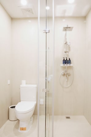 Un baño moderno con ducha separada por mampara de vidrio, inodoro y estante con artículos de aseo.