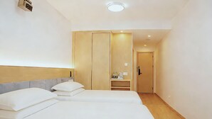 A hotel room with two beds, a wardrobe, a small kitchenette, and a door leading to another room.