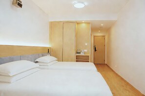 Habitación de hotel con dos camas, un armario, una kitchenette pequeña y una puerta que da a otra habitación.
