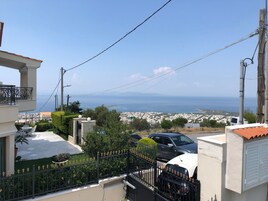 A residential area with a view of the sea, a white building with a balcony, and a black car parked in front.