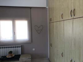 A room with a window, a radiator, a wooden bench, a potted plant, and a wardrobe.