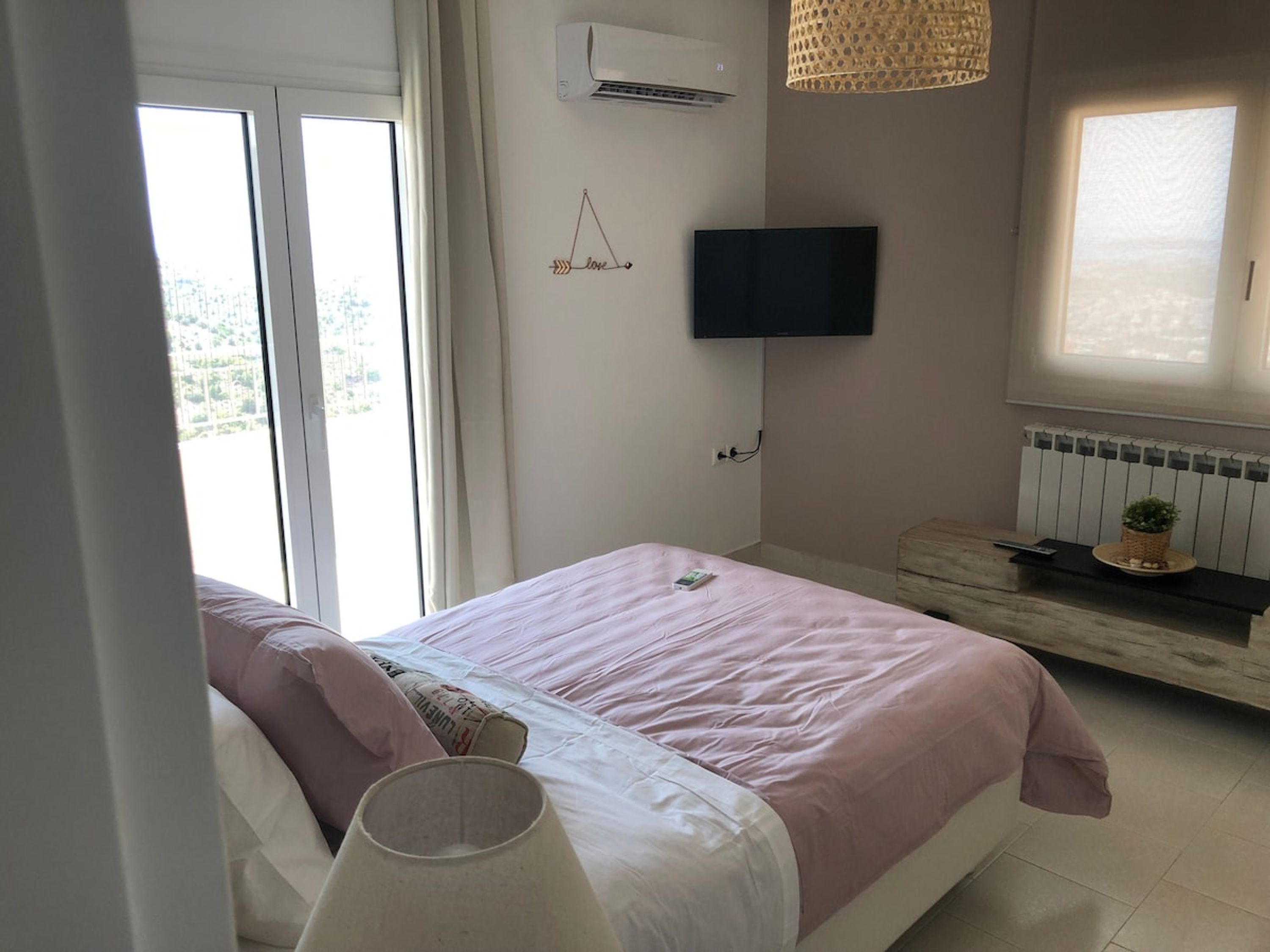 Un dormitorio con cama, televisor montado en la pared, ventana y radiador.