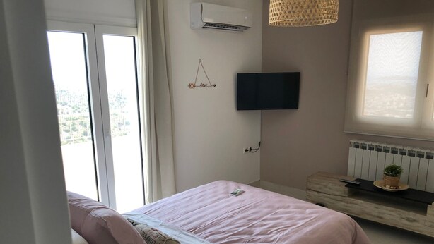 Un dormitorio con cama, televisor montado en la pared, ventana y radiador.