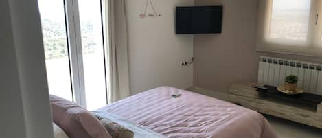 Un dormitorio con cama, televisor montado en la pared, ventana y radiador.