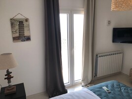 A bedroom with a bed, a TV, a radiator, a window with curtains, and a wall-mounted picture.
