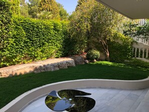 A curved outdoor seating area with a reflective surface, surrounded by a well-maintained garden with various plants and a stone wall. - Casa Panorama in Voula - Panoramic Sea View Villa (Vari-Voula-Vouliagmeni)