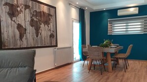 Una sala de estar moderna con un sofá, una mesa de comedor con sillas, una obra de arte con un mapa del mundo, un radiador y una ventana con persianas.