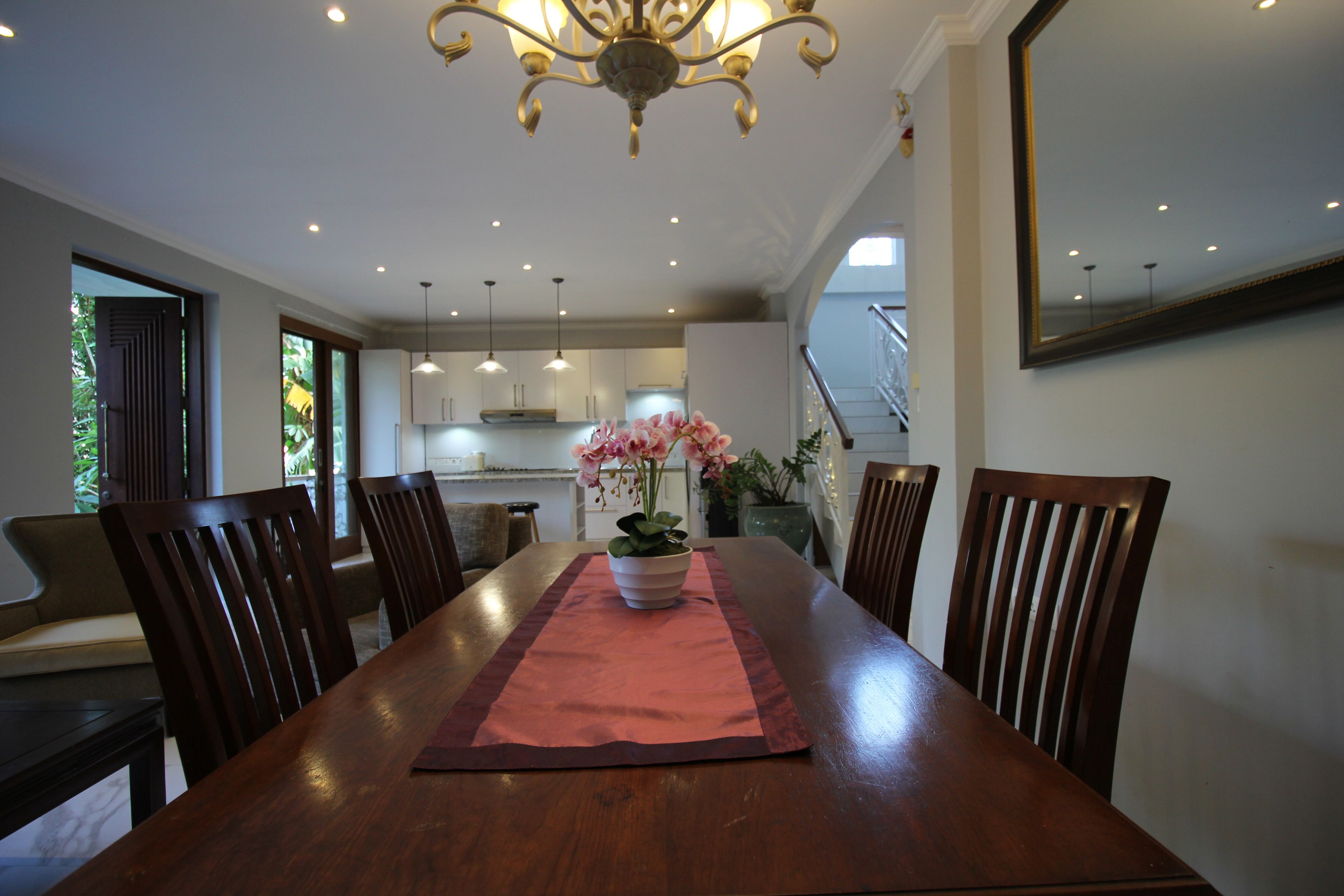 A dining area with a wooden table, chairs, a vase with flowers, and a chandelier.