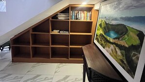 Una habitación con techo inclinado, una estantería de madera, un cuadro enmarcado y suelo de baldosas.
