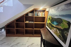 Ein Zimmer mit schrägen Wänden, einem hölzernen Bücherregal, einem gerahmten Gemälde und einem Fliesenboden.